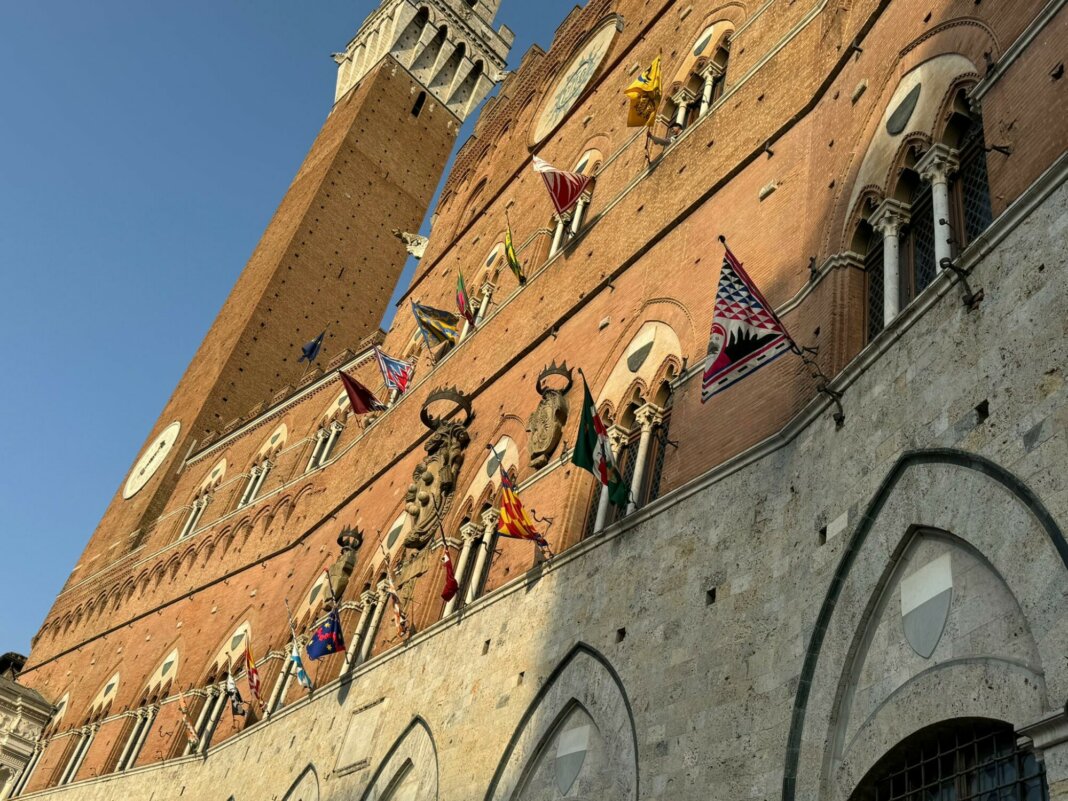 Le bandiere delle contrade esposte sulla facciata del palazzo pubblico di Siena